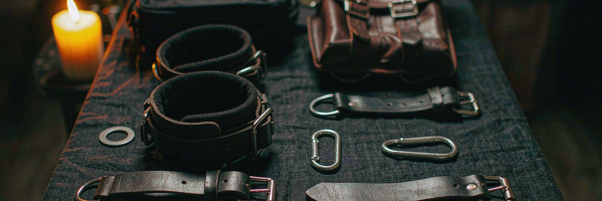 Beginner restraint set arranged in a neat grid: bed straps, plush cuffs and carabiners in candlelight