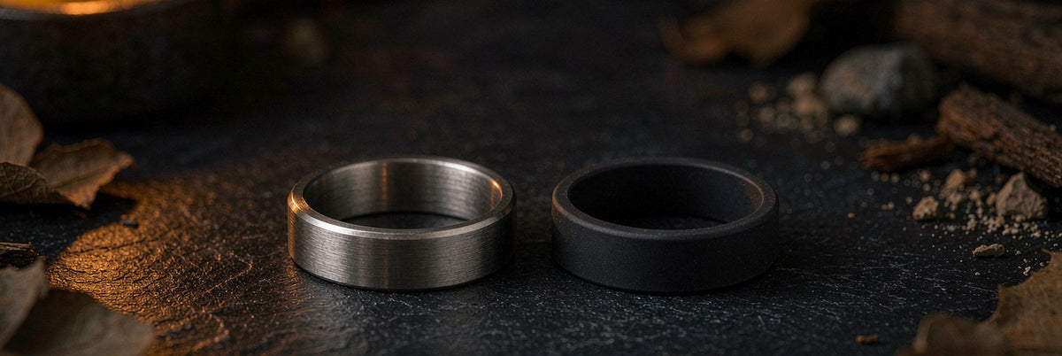 Brushed steel and matte black silicone rings side by side on dark slate in amber light
