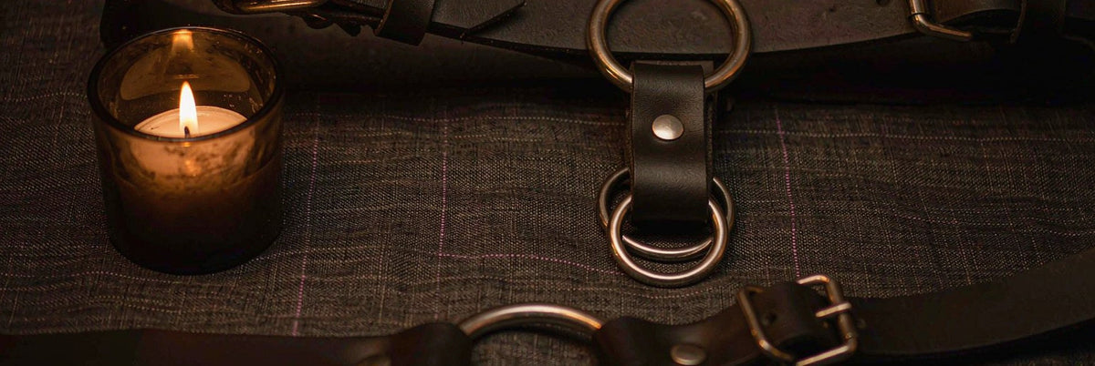 Black leather harness with steel O-rings arranged in symmetric flat lay on charcoal linen