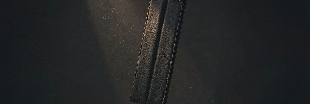 Black leather paddle under a single spotlight beam with drifting dust in a dark room