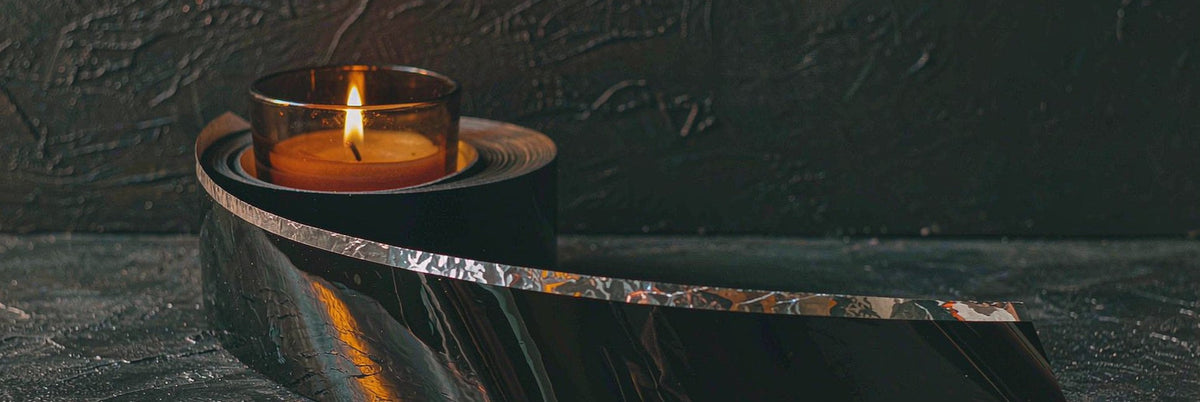 Glossy black bondage tape unspooled in an elegant curve across dark slate stone